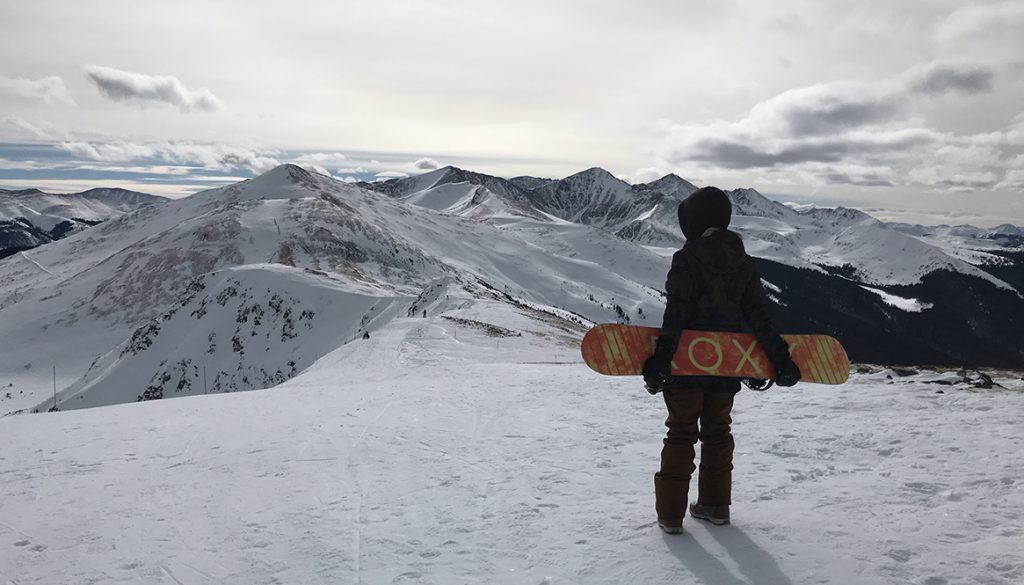 Stephanie Kemp on top of Peak 6 holding snowboard
