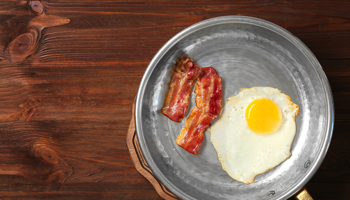 Delicious over easy egg with bacon in pan on wooden background